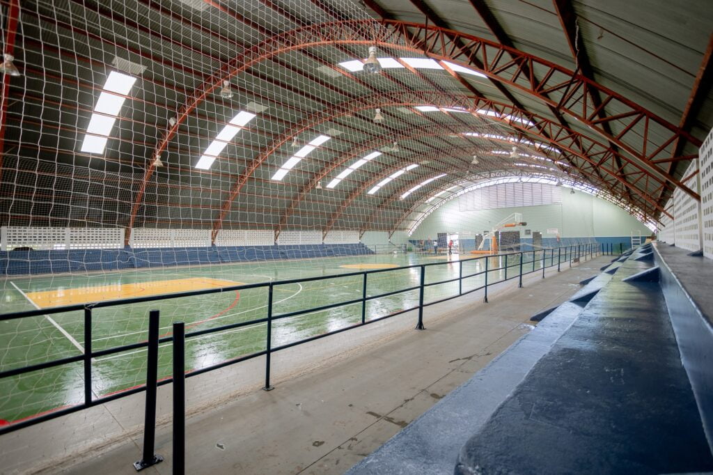 Imagem interna do ginásio, mostrando o telhado, as arquibancadas e a quadra