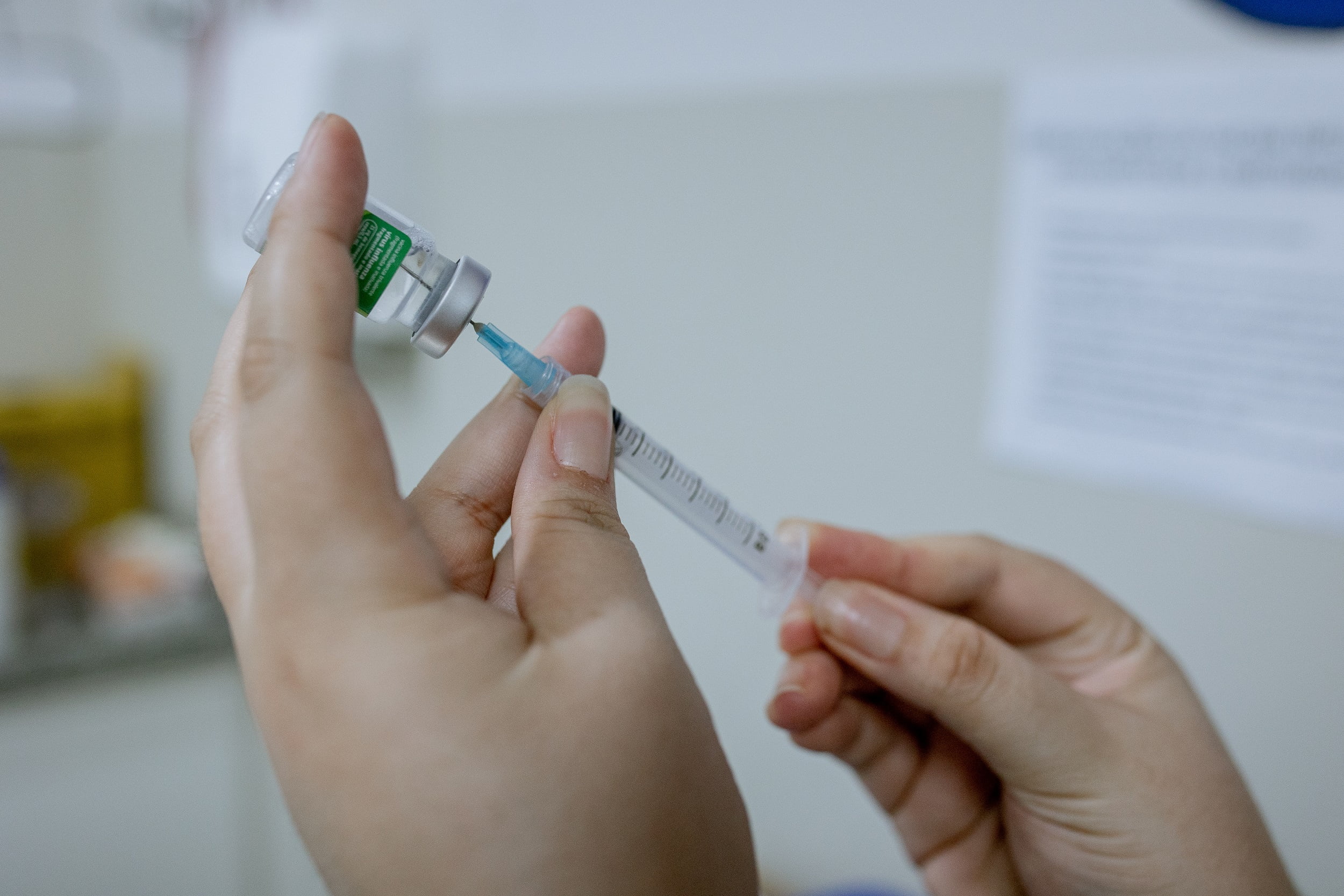 Imagem mostra as mãos da enfermeira que faz a fração da vacina da gripe em sala de vacinação em unidade de saúde pública