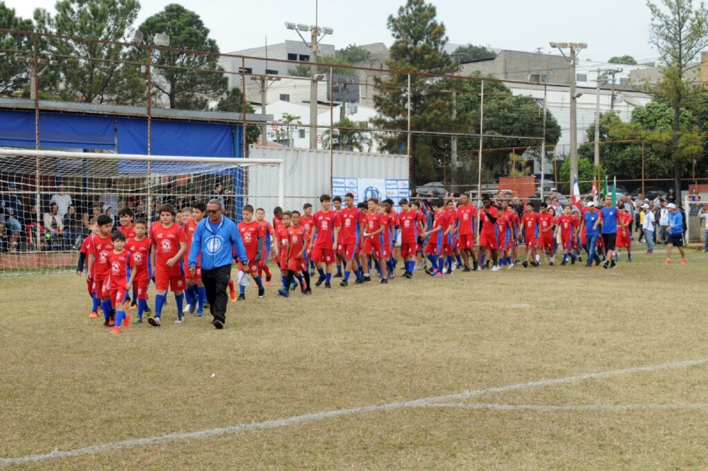 Jovens de uniforme vermelho desfilam pelo campo de futebol