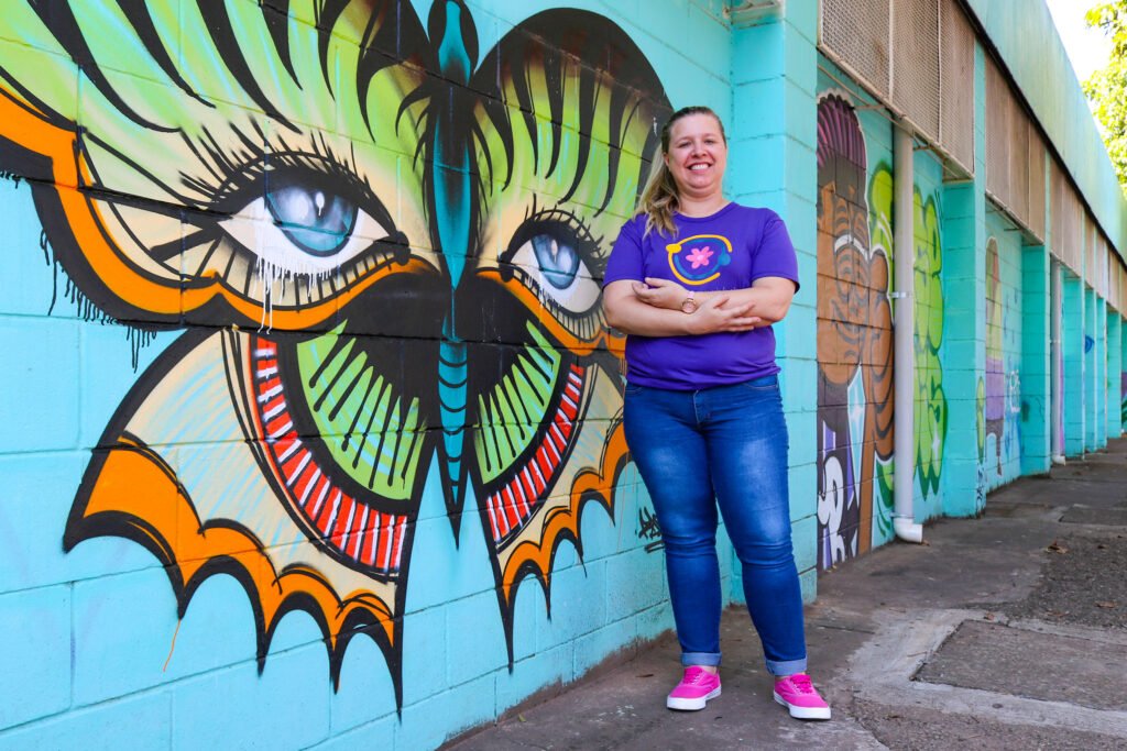 Imagem da coordenadora do CCInter, Vanessa Ometto, com muro grafitado ao fundo com um desenho de borboleta colorida