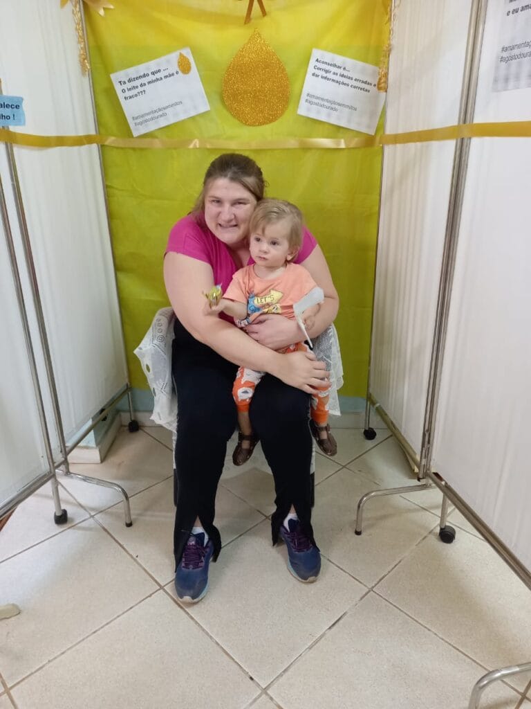 Sala está toda decorada de dourado com figuras alusivas ao aleitamento materno enquanto uma das mães amamenta seu filho