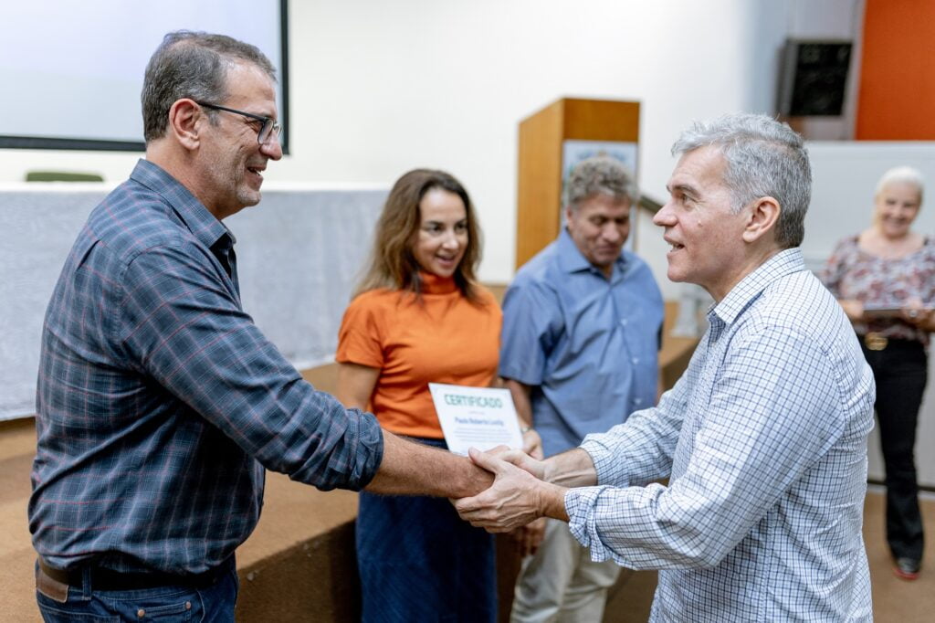 Imagem de duas pessoas em destaque, no primeiro plano da foto, sendo elas: aluno Paolo Gregori recebe certificado das mãos do prefeito Luciano Almeida