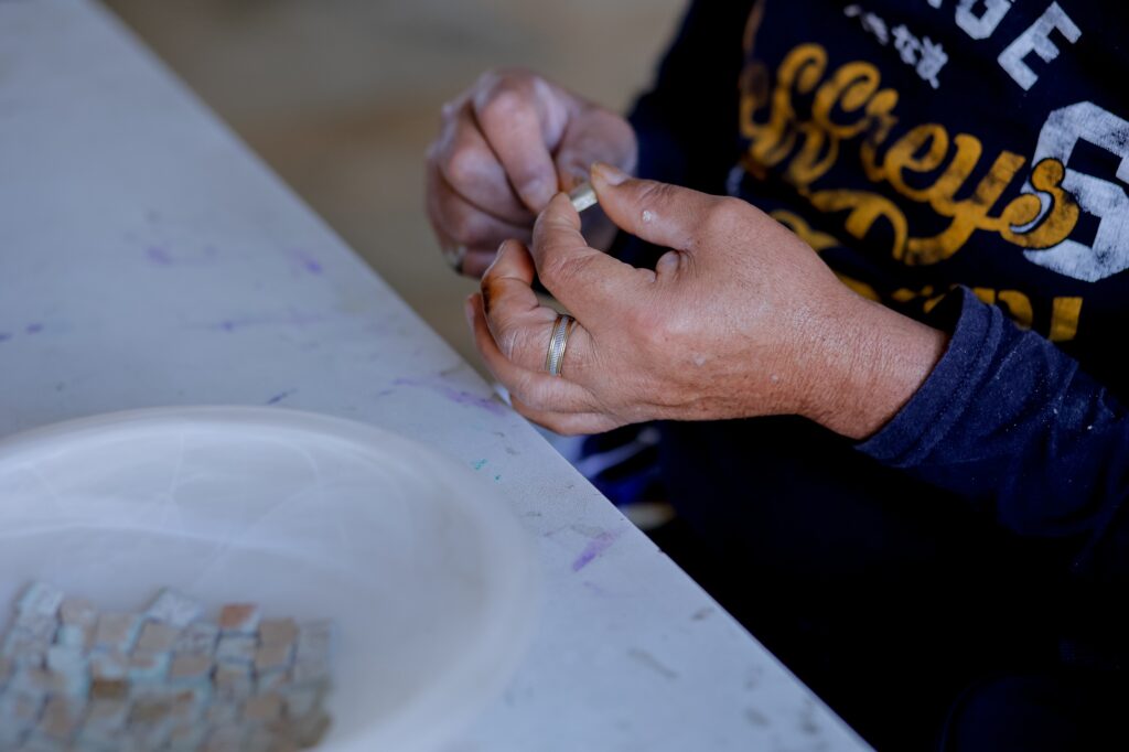 mãos do morador da SRT com resto de azulejo e cola para confecção de mosaico