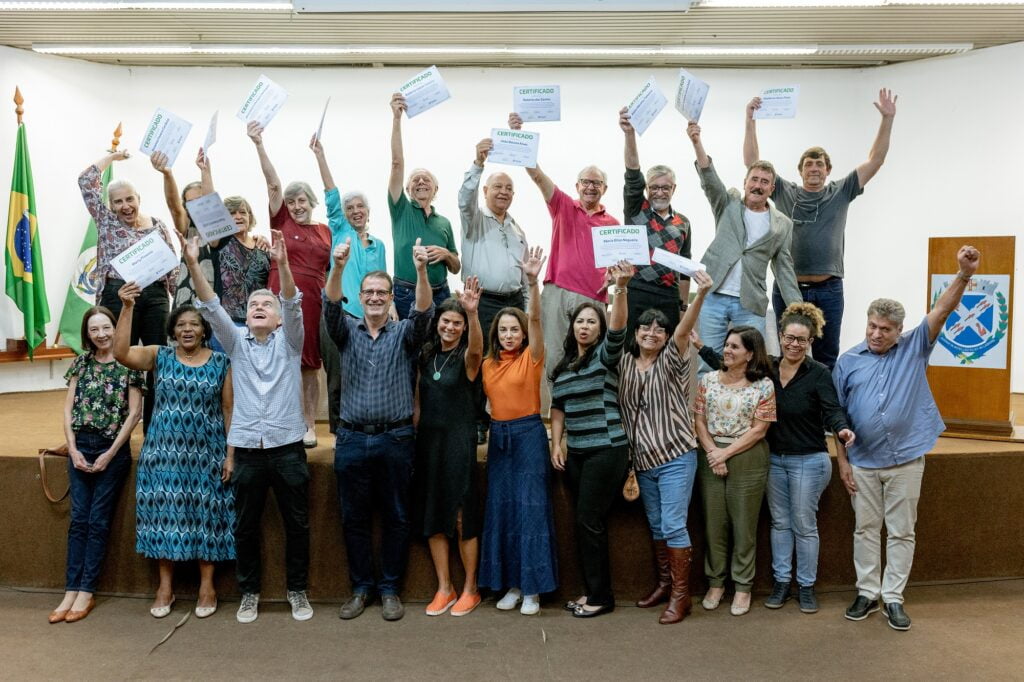 Imagem com os alunos do curso com os certificados levantados, expressando alegria