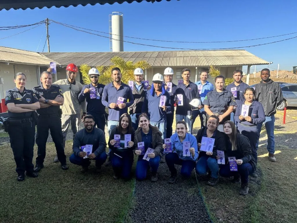 Equipe da Patrulha Maria da Penha de uniforme azul, junto com funcionários da construtora com folhetos lilás na mão