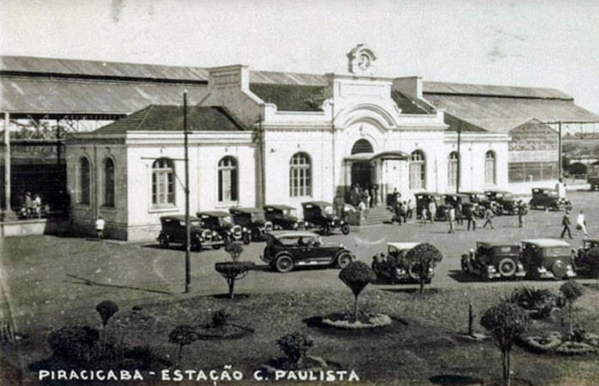 Imagem retrata antiga Estação da Paulista, com carros e diversas pessoas na frente do prédio. Foto em preto e branco.