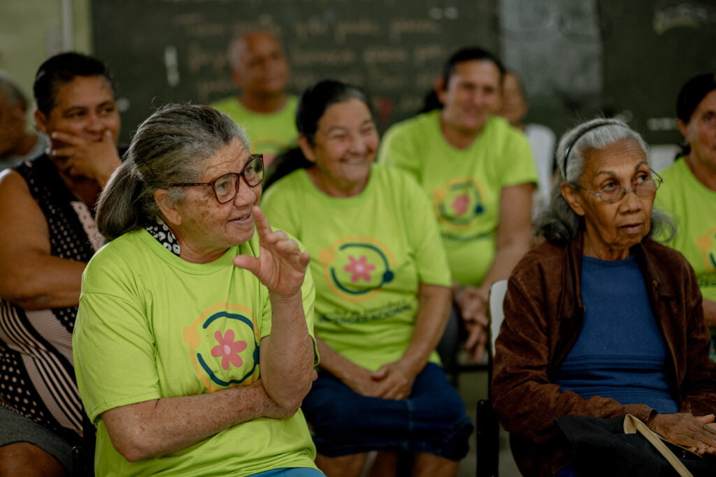 Na imagem, pessoas idosas sentadas, rindo durante a oficina sobre Elias dos bonecos
