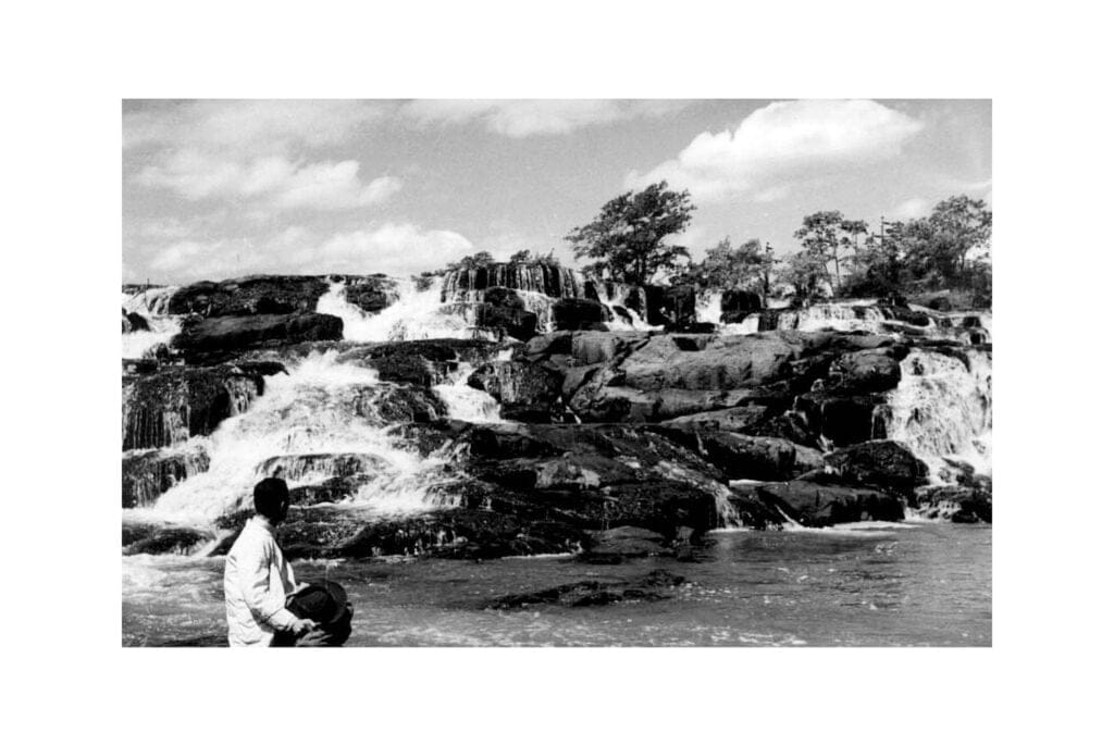 Homen sentado observa o movimento da água nas pedras  do Rio Piracicaba