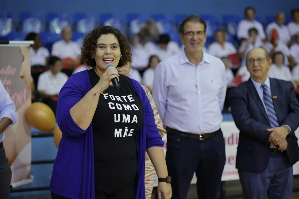 Mulher de azul com microfone na mão, ao lado do prefeito Luciano Almeida