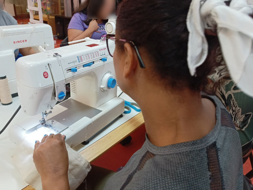 Na foto, imagem desfocada de mulher usuária do Cram, operando máquina de costura