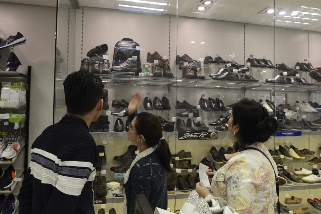atendente mostra sapatos na vitrine e agente do Procon, com papel na mão, observa