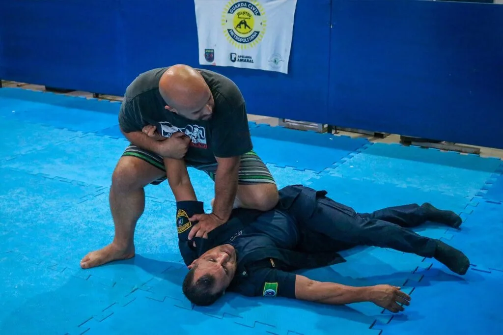 Homem careca que é o instrutor, imobiliza um guarda civil, de uniforme escuro