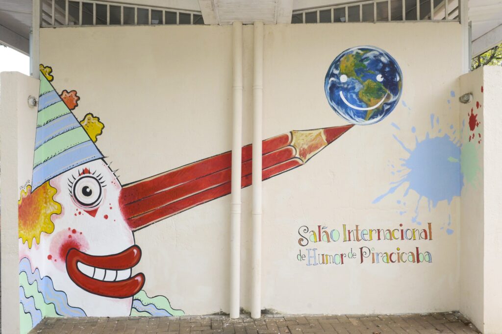 Imagem feita pelo artistas retrata um palhaço que, no lugar do tradicional nariz vermelho, possui um lápis equilibrando, em sua ponta, o globo terrestre sorrindo