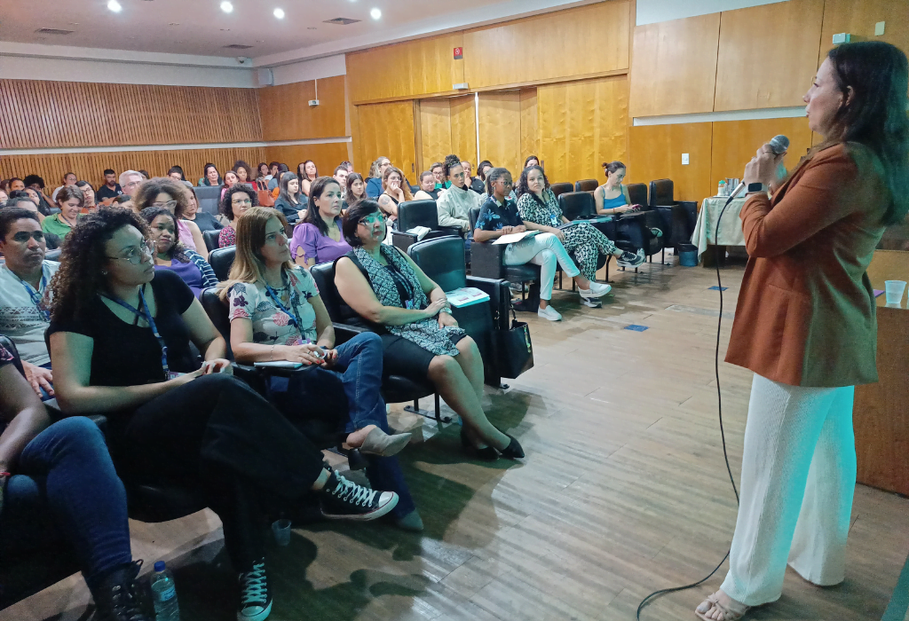 Na imagem, participantes da palestra sentados à esquerda e à frente, Fabiana Menegon palestrando