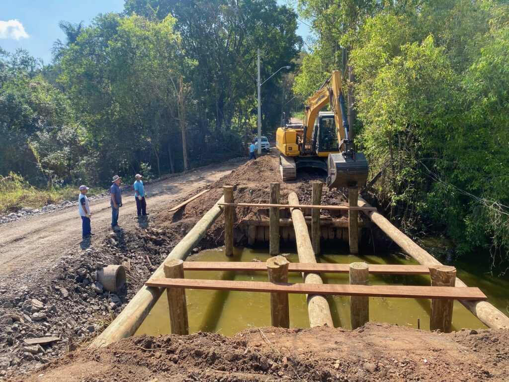 Escavadeira da Sema fazendo a reconstrução da ponte com madeiras de eucalipto tratado e equipe ao lado auxiliando