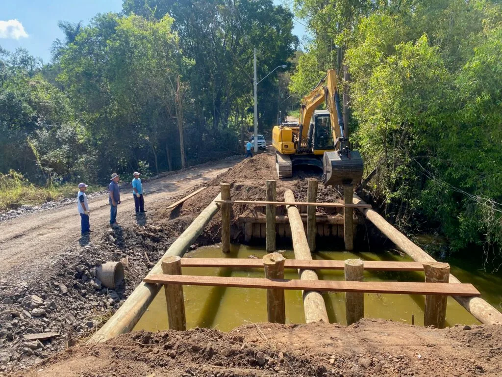 Escavadeira da Sema fazendo a reconstrução da ponte com madeiras de eucalipto tratado e equipe ao lado auxiliando