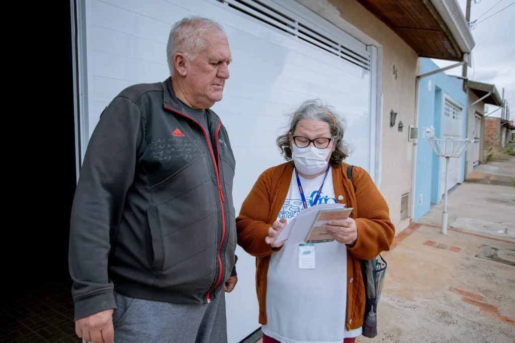 Morador Roberto Pisani recebe orientações da agente de saúde Neusa em frente da sua casas. Neusa mostra ao Roberto folhetos com informações sobre prevenção a acidentes com escorpiões
