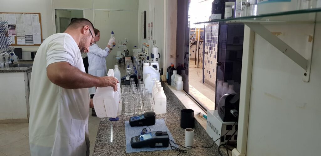 Imagem de dois trabalhadores com roupa branca fazendo análises no laboratório