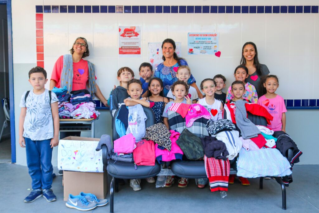 Imagem de crianças atrás de uma bancada com roupas arrecadas pela escola Joaquim Carlos para a Campanha do Agasalho
