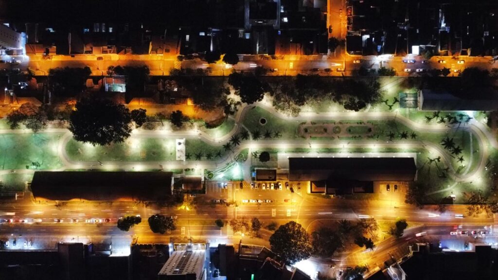 Imagem aérea do bairro Paulista a noite, mostra casas, prédios, carros nas ruas e luzes. Em destaque, a Estação da Paulista iluminada com as novas luminárias