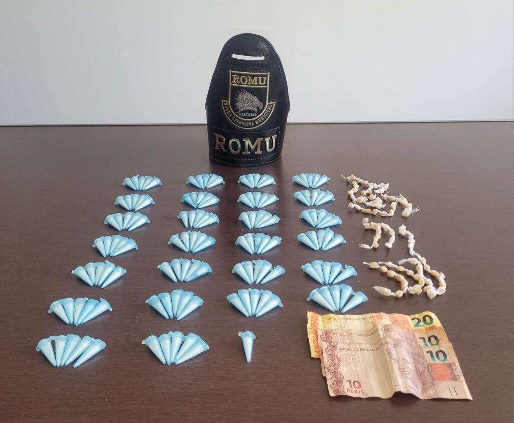 Em uma mesa marrom de madeira, equipe da guarda civil exibe as drogas e o dinheiro apreendidos com o suspeito