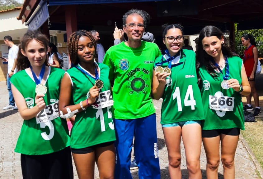 Técnico e atletas, todos vestidos com roupas verdes, estão sorrindo e felizes após a conquista da medalha, em São Carlos.