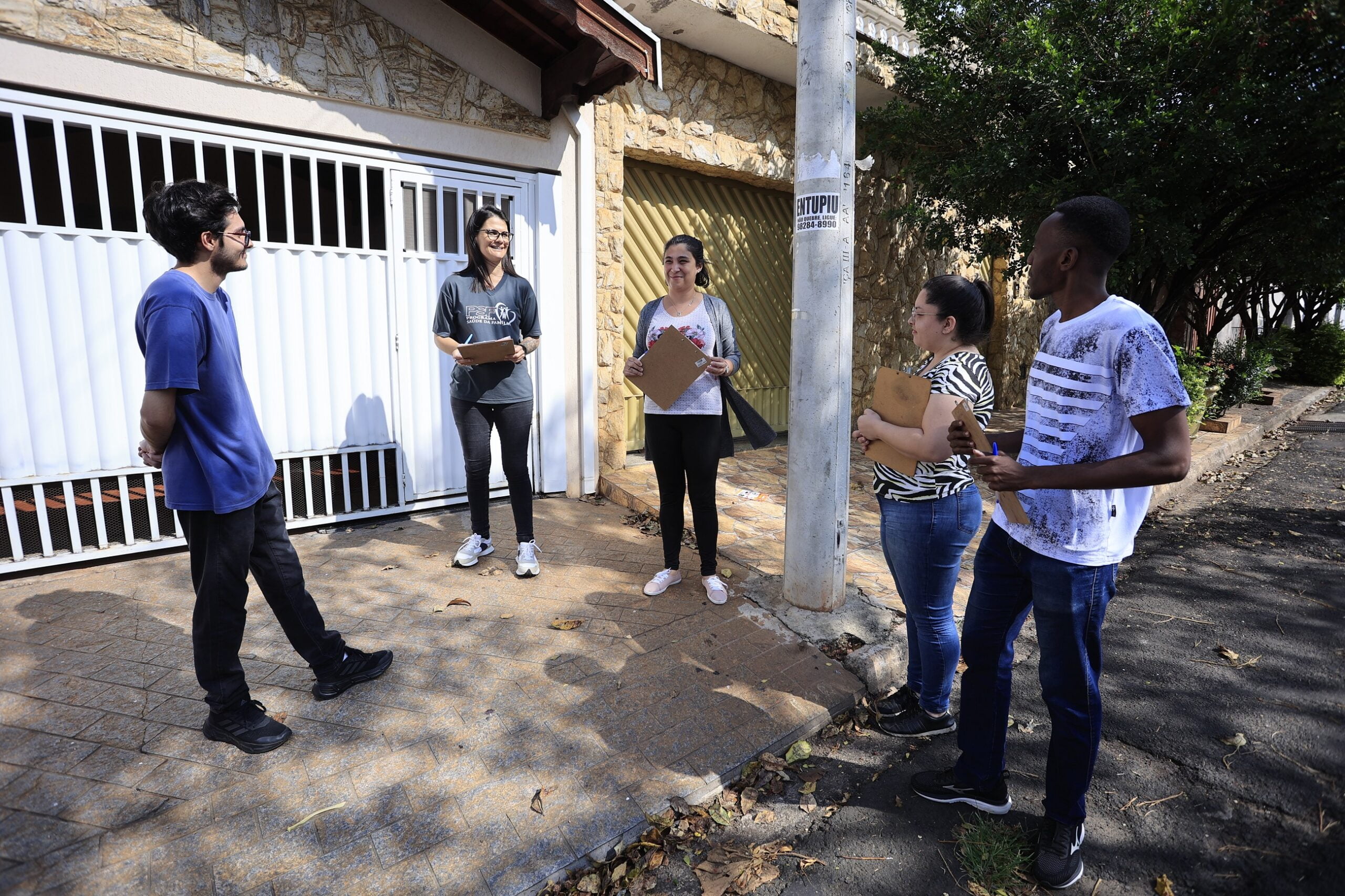 Em frente a uma casa amarela de portão branco parte dos agentes de saúde estão em treinamento na região do PSF Astúrias