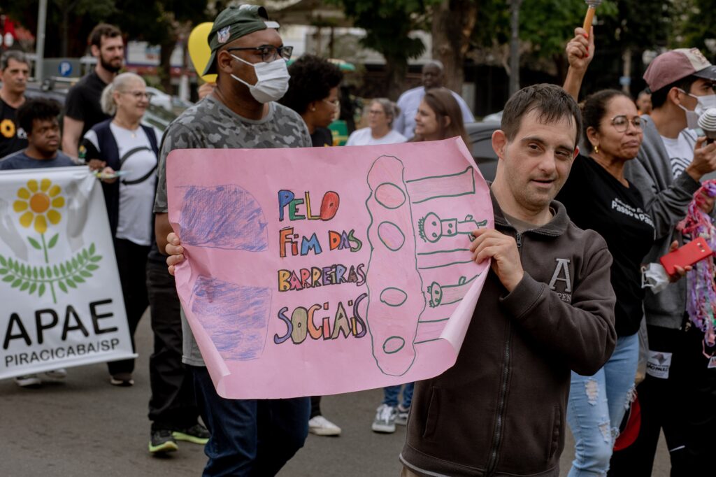 Na imagem, pessoas carregam cartazes durante a caminhada inclusiva de 2022