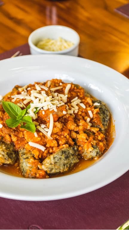 imagem de nhoque de chicória com molho e queijo por cima