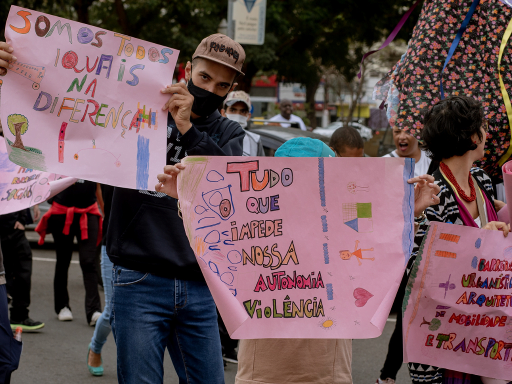 Na imagem, pessoas carregam cartazes com frases de inclusão