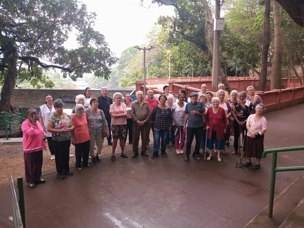 Na imagem, pessoas idosas em pé ao centro. Atrás, árvores e colunas do Parque do Mirante