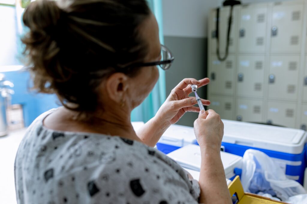 Enfermeira com seringa nas mãos faz a dosagem de vacina para aplicação em criança