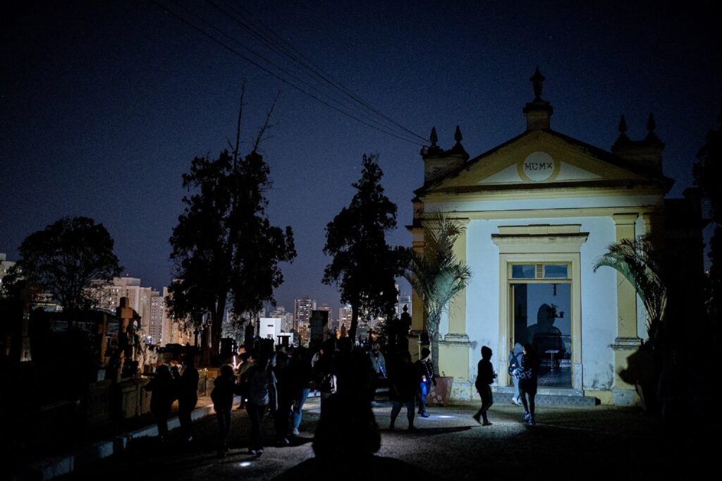 Pessoas no escuro visitando o cemitério da Saudade.