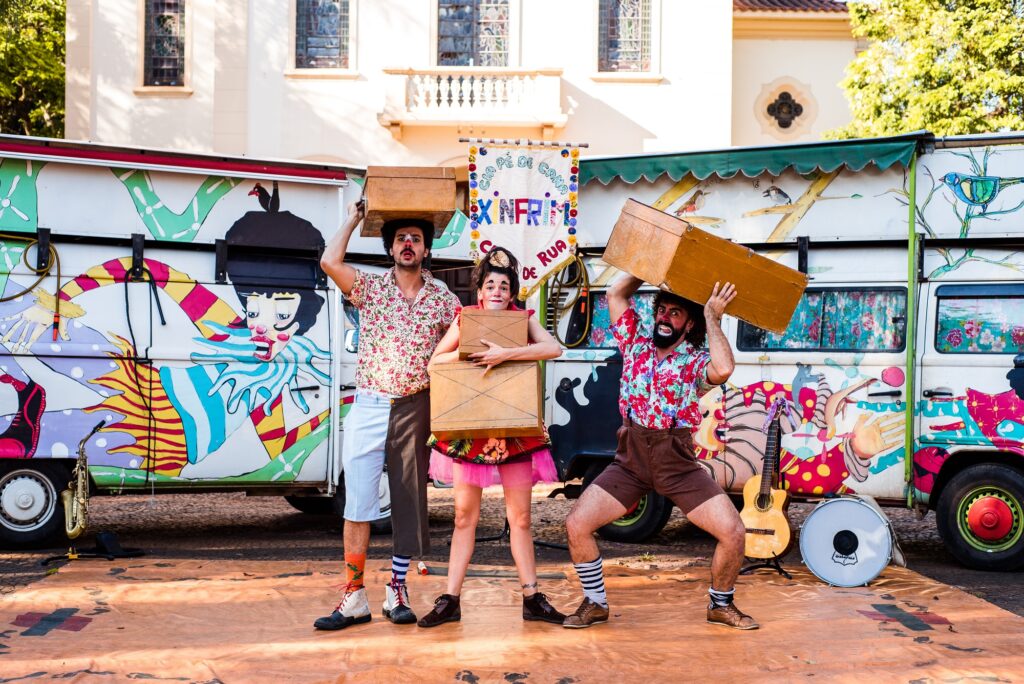 uma mulher entre dois homens com figurinos circenses