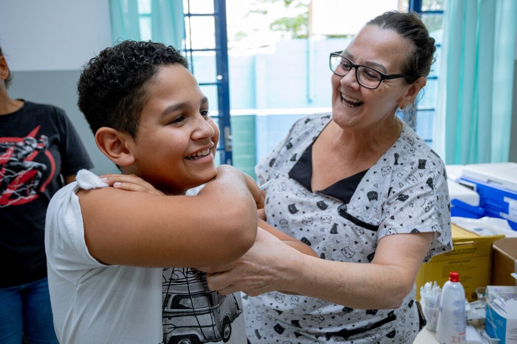 O menino Davi Oliveira soridente recebendo a vacina