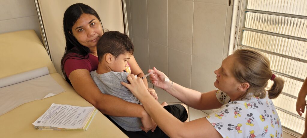 Diego de Assis, de cinco anos, recebe dose de vacina no colo da mãe Thais