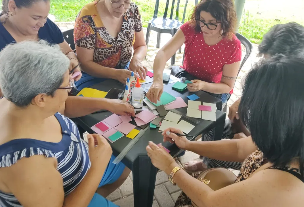 Idosos e familiares em volta da mesa, em atividade com papel recortado para ativar a memória