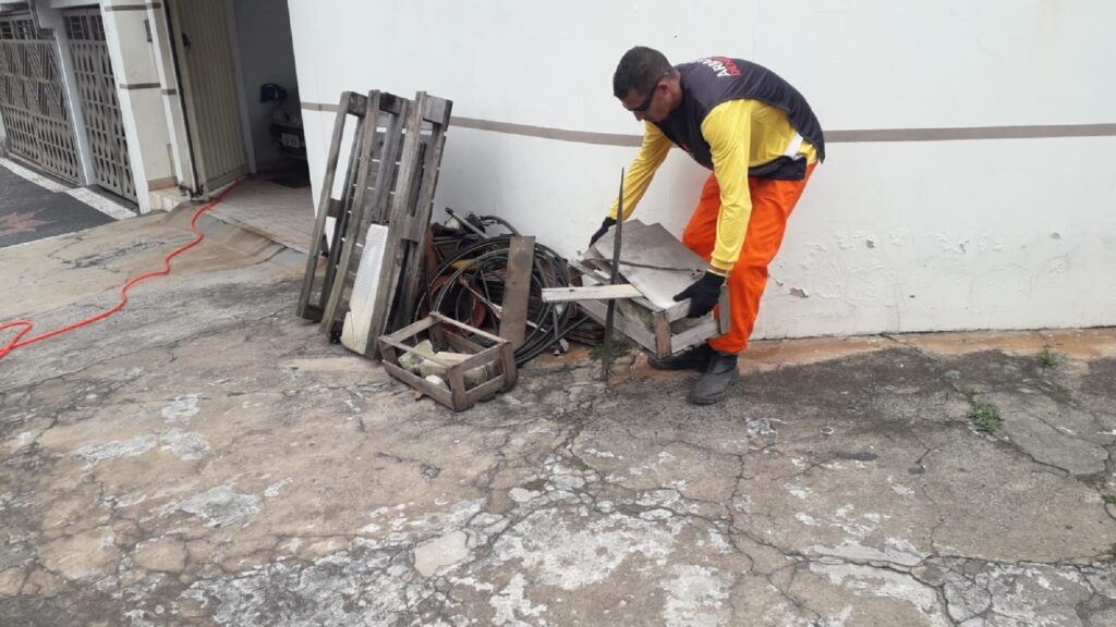 Homem de uniforme nas cores preto, amarelo e laranja, recolhe inservíveis colocados na calçada.
