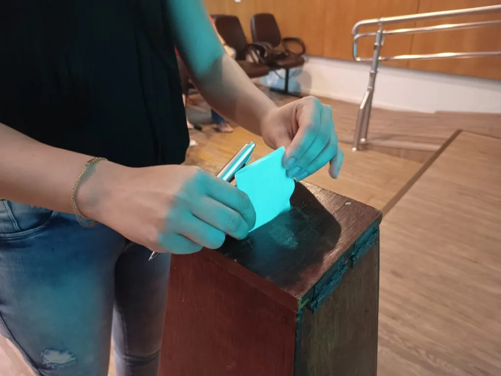 Imagem ilustrativa de mãos colocando voto impresso dentro de urna.