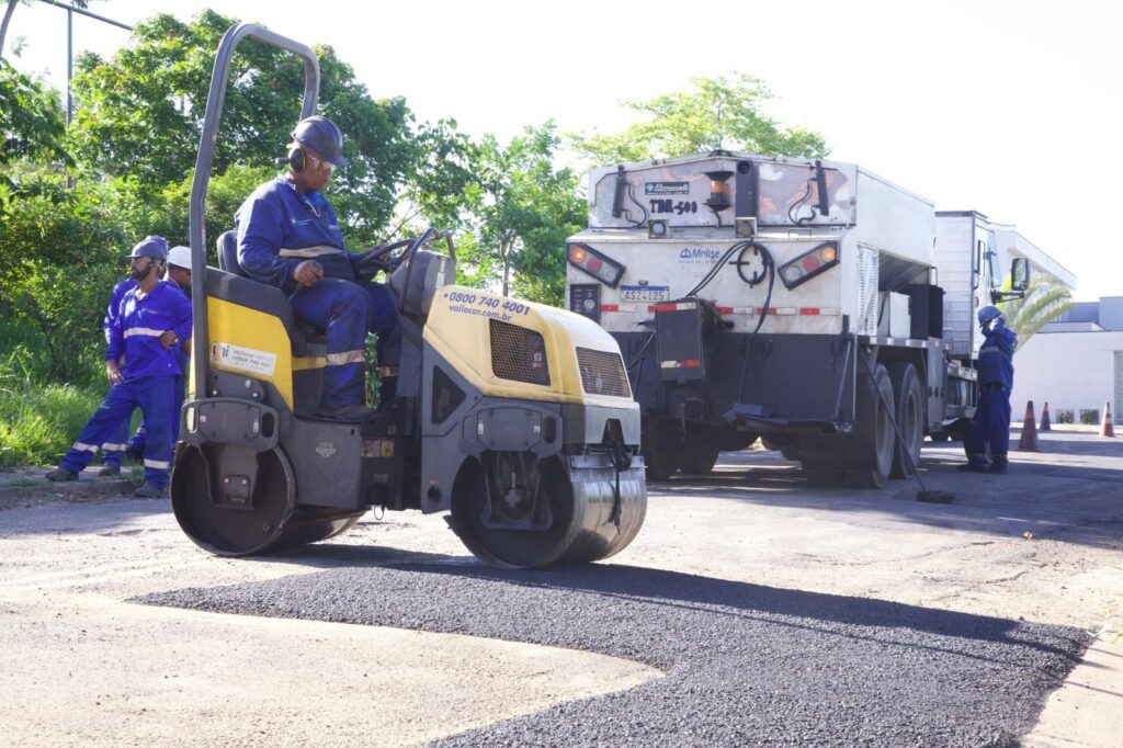 homens trabalhando na aplicação de asfalto, com destaque para homem em máquina ajeitando a nova camada de asfalto