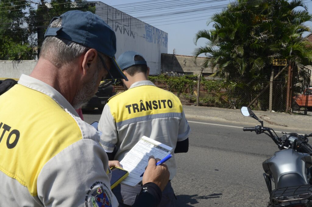 homens em pé, fazendo anotações, com uniforme da secretaria de trânsito