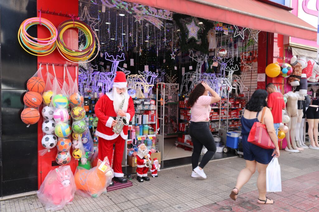 Boneco do Papai Noel toca instrumento musical em frente a loja