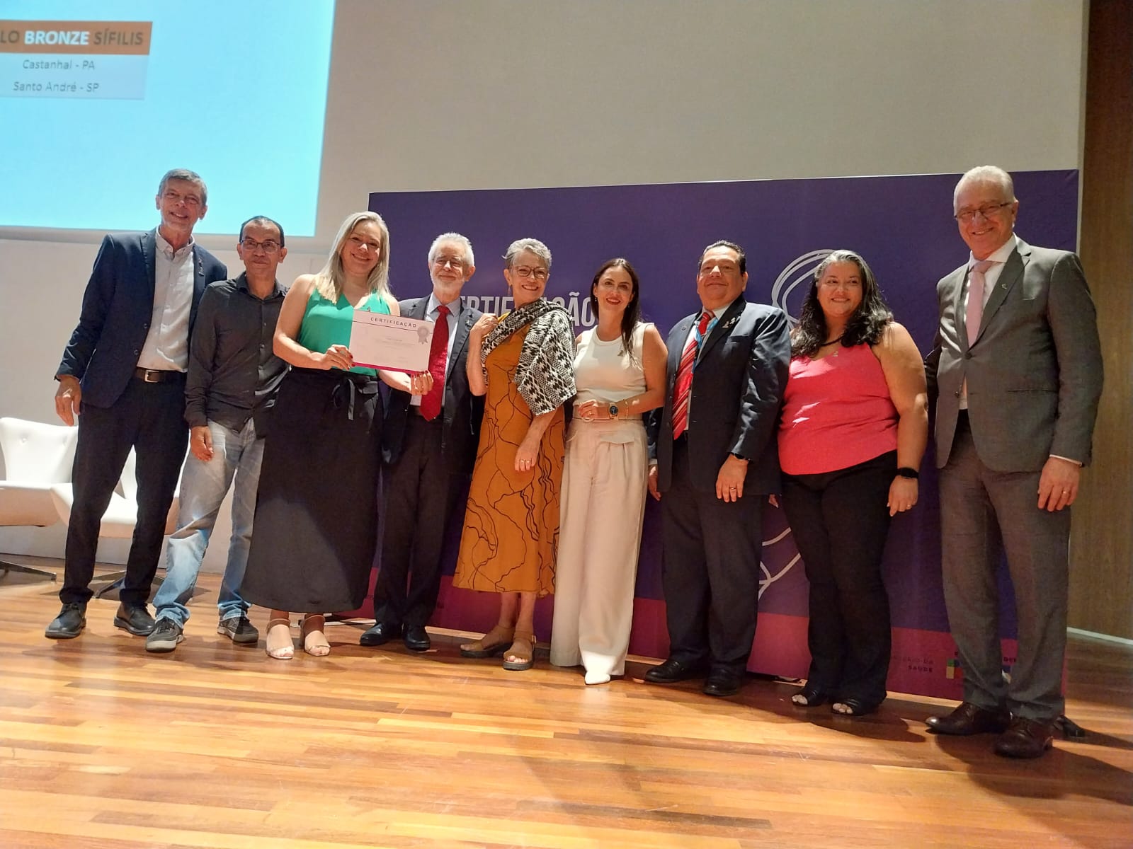 Karina, vestida de verde, recebe certificado de boas práticas em nome da prefeitura das mãos de representantes do Ministério da Saúde