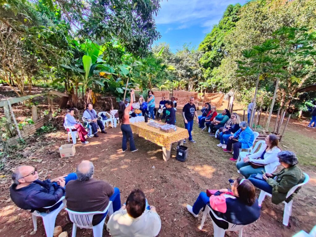 Na imagem, pessoas idosas sentadas em círculo em meio à natureza e ao centro, monitores falam sobre ecologia 