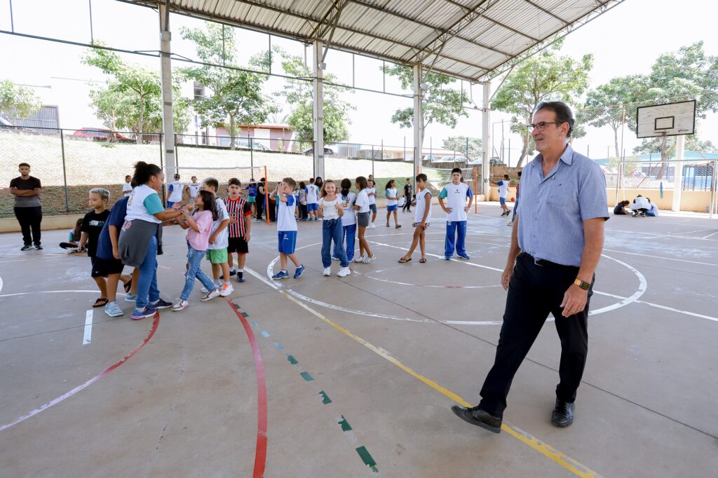 homem em pé caminhando em quadra de escola com diversas crianças 