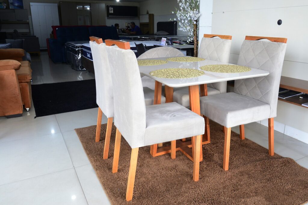 Mesa quadrangular branca com detalhes laranja, exposta em loja de decoração.e quatro cadeiras.