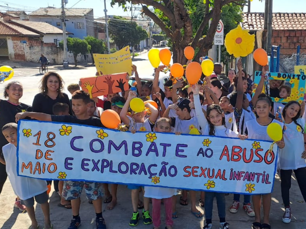 Na imagem, crianças, adolescentes seguram faixa com os dizeres: combate ao abuso e exploração sexual de crianças e adolescentes
