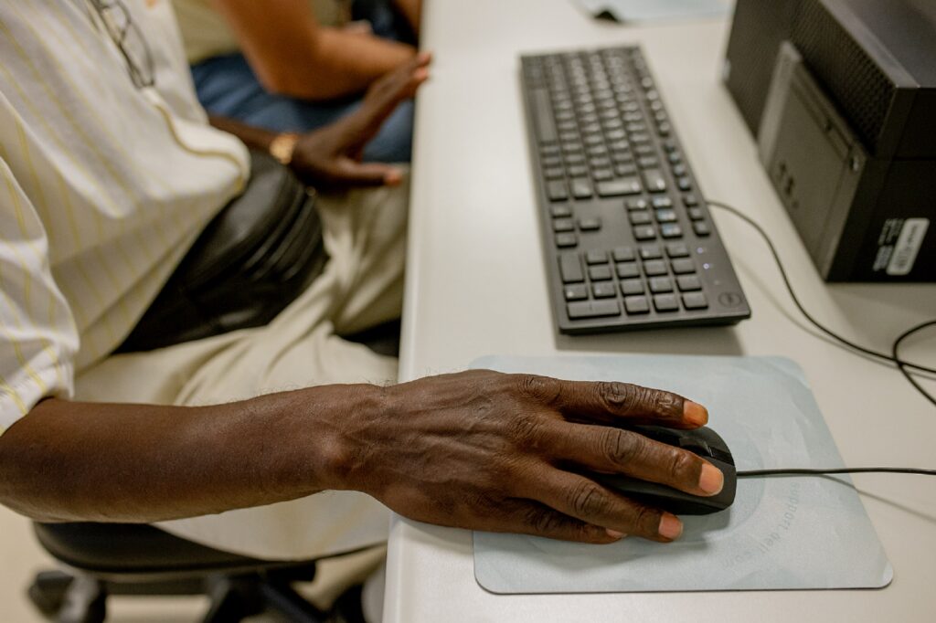 Uma mão segura o mouse p´roximo ao teclado do computador, ilustrando um curso de qualificação profissional