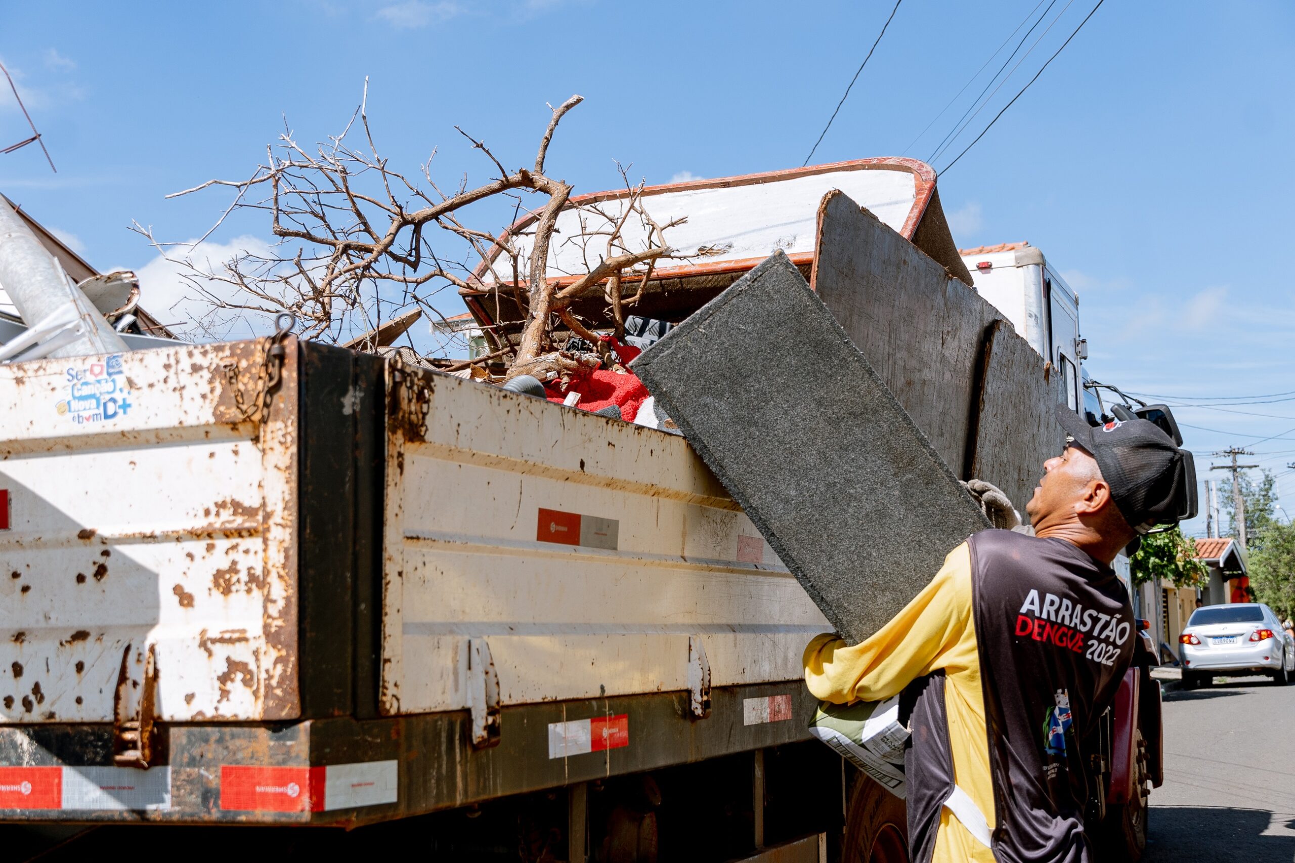 imagem mostra carroceria do caminhão da prefeitura cheio de materiais inservíveis; um servidor está com materiais na mão e faz o movimento para cima arremessando o material para dentro da carroceria