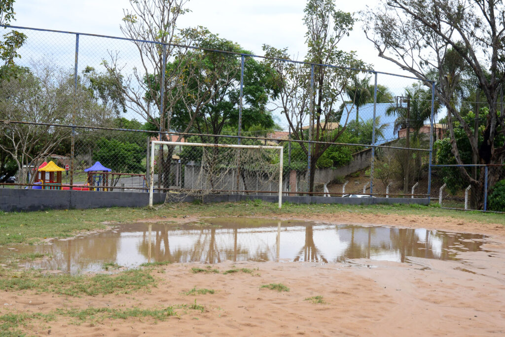 Quadra de areia da Estância Lago Azul, em Artemis. A quadra está vazia e alagada com as chuvas. Na imagem, apenas uma trave com redes rasgadas e um parquinho infantil, bem mais ao fundo. 